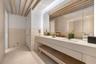 Dual vanity with integrated sinks, stone-surface countertop, full-width mirror with integrated lighting, exposed wood ceiling beams, and stone-finish 
