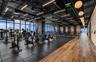 Fitness center featuring floor-to-ceiling windows, exposed industrial ceilings with recessed lighting, wood-finish flooring, and a textured brick acce