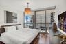 Floor-to-ceiling windows, wood-finish flooring, sliding glass door access to a private balcony, and a multi-tiered drum pendant light fixture