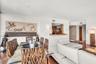 Open-concept living space featuring wood-finish flooring, a pass-through kitchen window with a built-in wooden ledge, wall-mounted light fixtures, and
