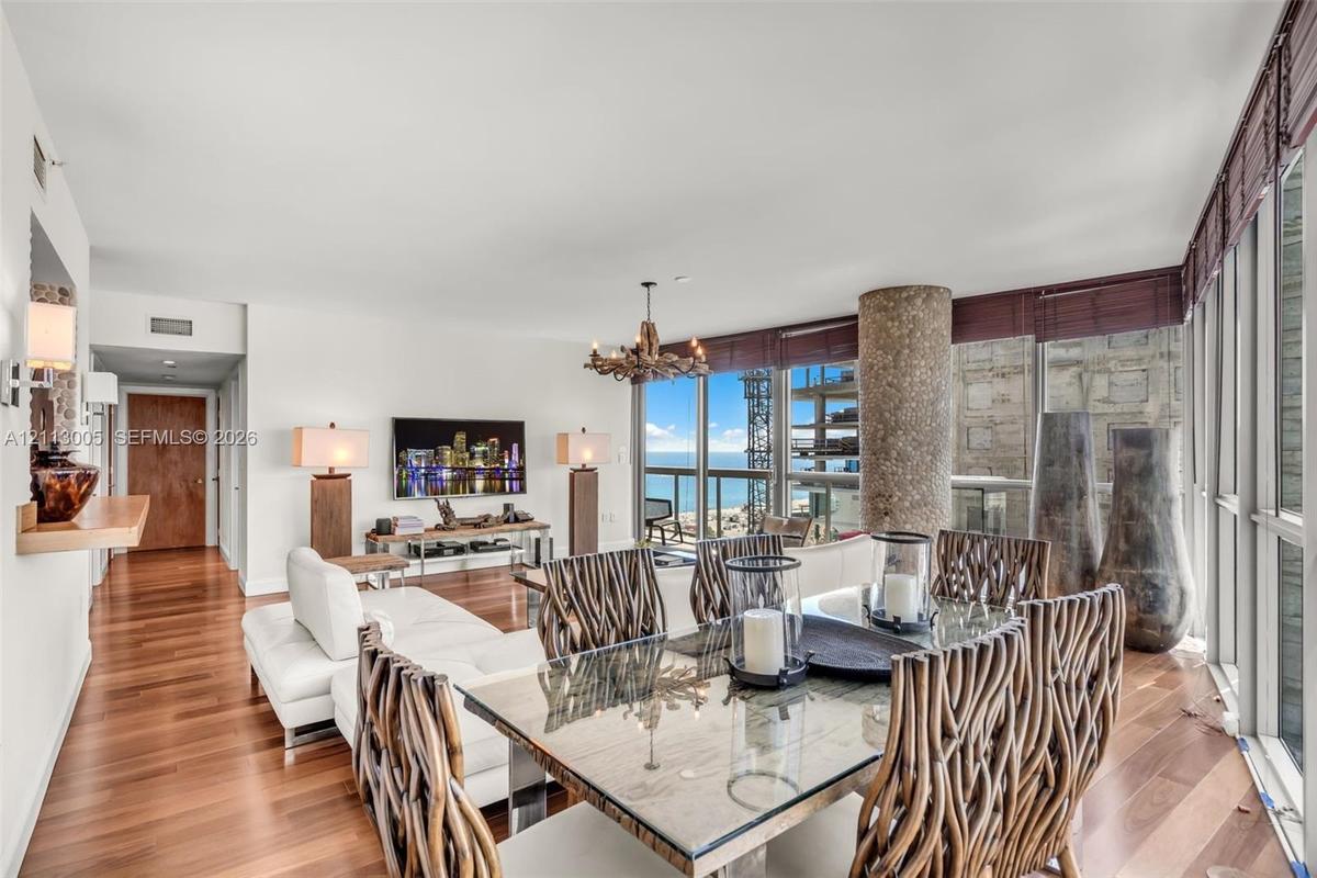 Open-concept interior featuring floor-to-ceiling windows, wood-finish flooring, a textured stone-clad support column, and custom chandelier lighting