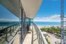 Expansive private balcony featuring stone flooring, a glass panel railing, floor-to-ceiling glass wall, and coastal scenery