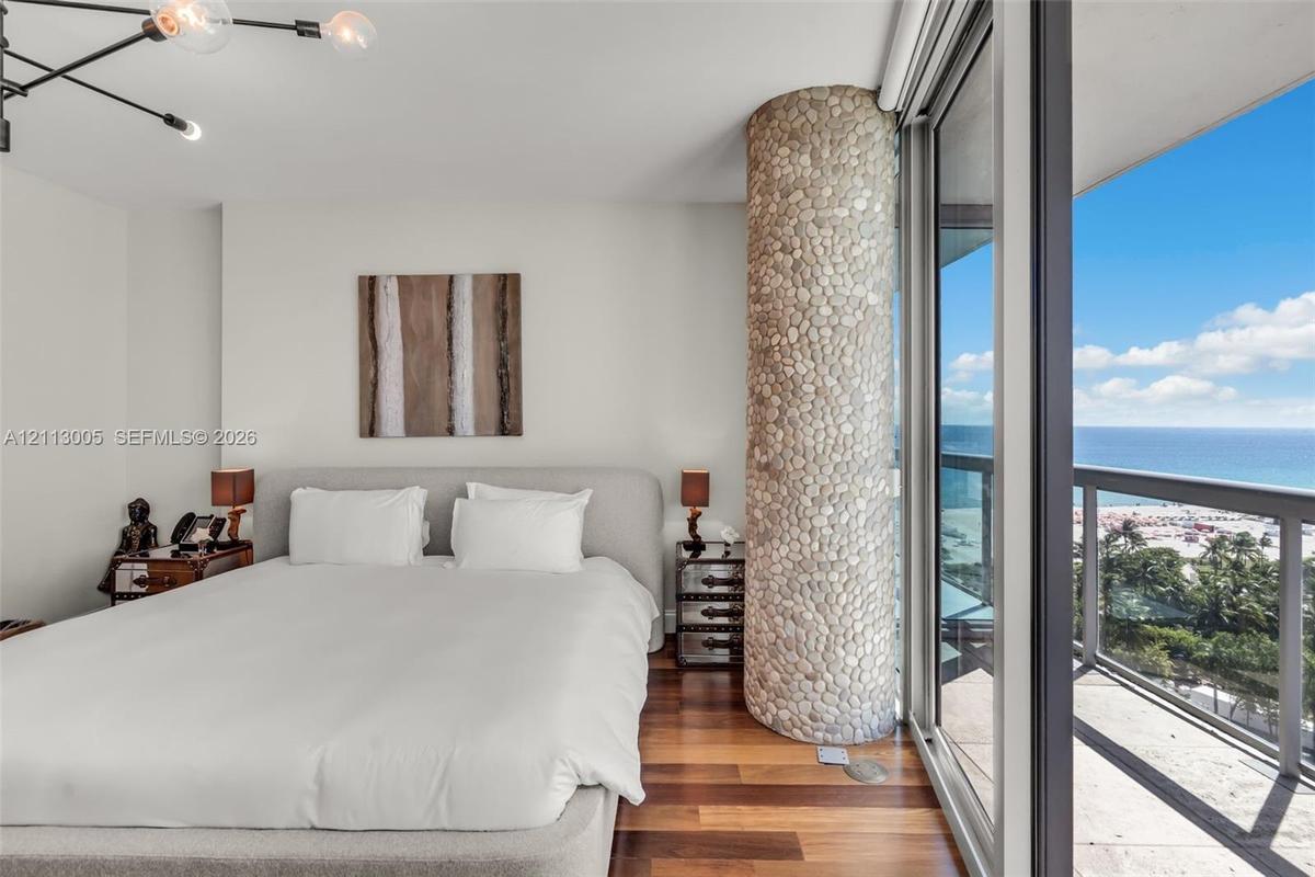Floor-to-ceiling sliding glass doors opening to a balcony, natural stone-clad architectural pillar, wood-finish flooring, and modern multi-arm ceiling