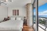 Floor-to-ceiling sliding glass doors opening to a balcony, natural stone-clad architectural pillar, wood-finish flooring, and modern multi-arm ceiling