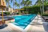 Rectangular swimming pool featuring a stone-tile deck, metal handrails, and surrounding manicured hedges