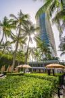 High-rise building with tiered balcony architecture, surrounding palm trees, and manicured green hedges