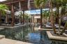 Expansive courtyard featuring a reflection pool, overhead wood-slat pergola, integrated palm tree planters, stone tile hardscaping, and built-in mason