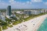Aerial perspective of coastal high-rise development featuring direct oceanfront access, extensive white sand shoreline, and proximity to regional metr