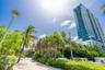 High-rise residential tower featuring blue glass cladding and tiered balconies, situated along a landscaped pedestrian walkway with mature palm trees 