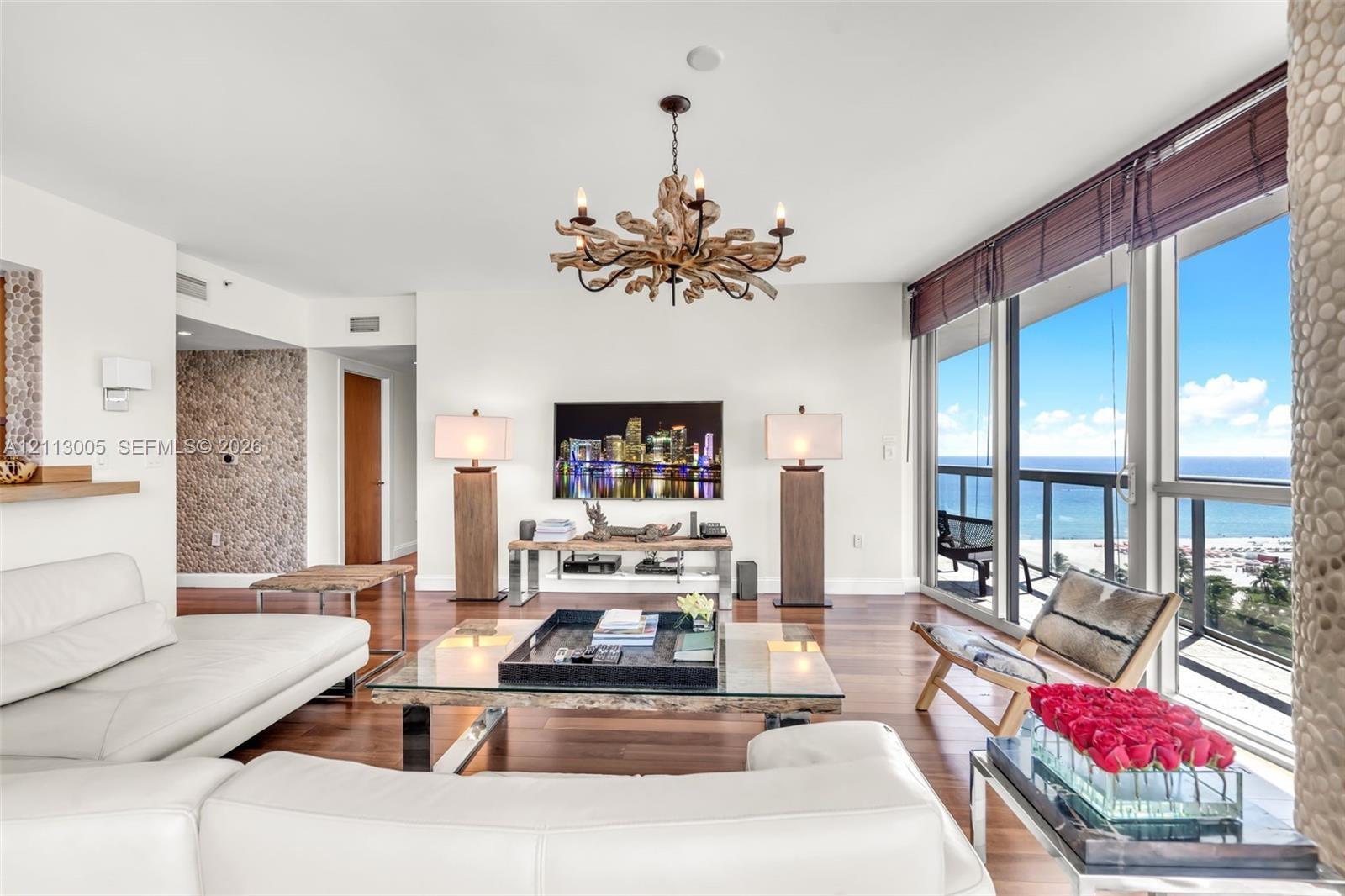 Living area featuring floor-to-ceiling windows, wood-finish flooring, decorative stone-textured wall accents, and an intricate statement chandelier