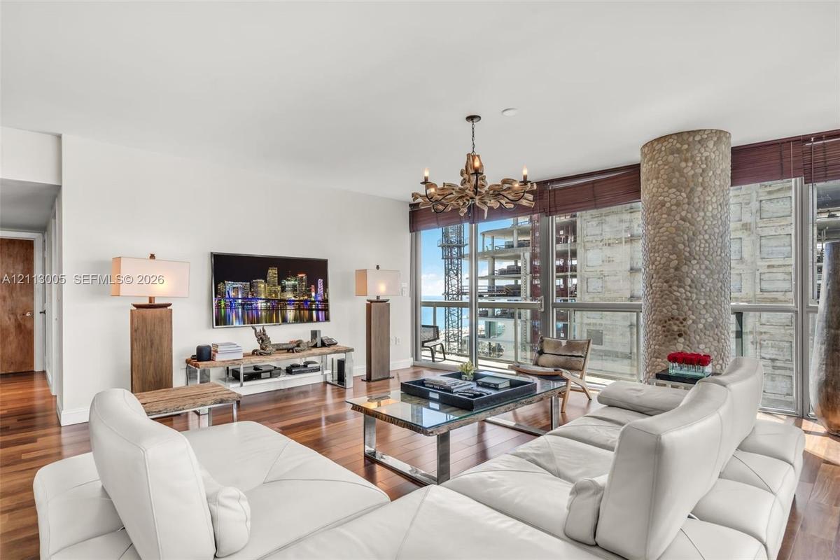 Living area featuring wood-finish flooring, floor-to-ceiling windows, a decorative stone-clad structural column, and a multi-arm chandelier