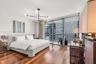 Floor-to-ceiling windows, wood-finish flooring, exposed textured structural column, multi-arm geometric light fixture, and glass sliding door access t