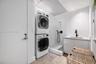 Laundry area featuring stacked appliances, tiled shower enclosure with handheld sprayer, built-in cabinetry, solid-surface countertop, and matte black