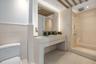 Stone-surfaced floating vanity, ceiling with exposed wood-finish beams, integrated medicine cabinet, and glass-enclosed walk-in shower with stone tile