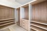 Custom walk-in closet featuring wood-finish cabinetry, built-in shelving, integrated hanging rods, and a three-drawer storage unit with matte black ha