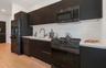 Modern kitchen featuring matte black flat-panel cabinetry, white solid surface countertops, white subway tile backsplash, and a suite of black applian