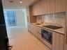 Kitchen featuring flat-panel wood-finish cabinetry, integrated appliances, light-toned stone-patterned backsplash, and ceramic tile flooring