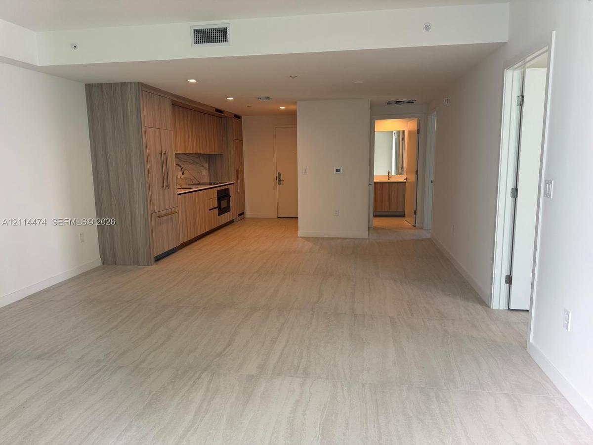 Open-plan living area featuring wood-finish cabinetry, stone-patterned backsplash, recessed lighting, and tile flooring