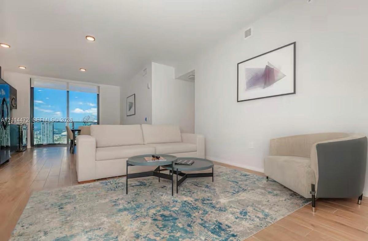 Open-concept living space featuring wood-finish flooring, recessed lighting, and floor-to-ceiling glass paneling with balcony access