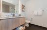 Floating vanity with wood-finish cabinetry and light-toned countertop, large rectangular mirror with integrated LED lighting, matte black fixtures, an