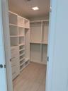 Walk-in closet featuring white built-in shelving, integrated dresser drawers with metal hardware, double-tier hanging rods, and wood-finish flooring