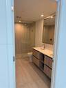Bathroom featuring a floating vanity with wood-finish cabinetry, solid-surface countertop with dual under-mount sinks, gold-tone hardware, and a walk-
