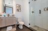 Wood-finish floating vanity with an integrated countertop, illuminated wall-mounted mirror, walk-in shower with white subway tile surround, and large-