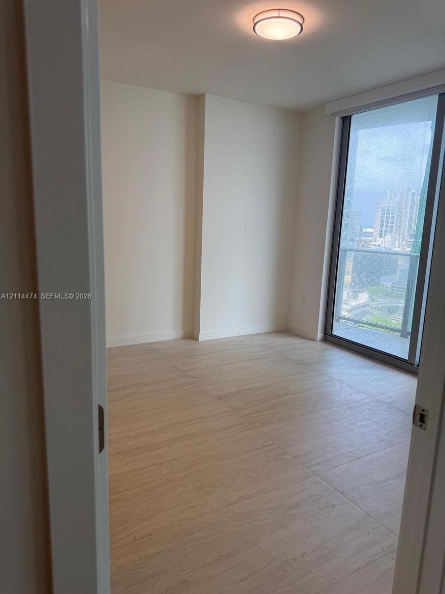 Neutral-toned interior featuring wood-finish flooring, floor-to-ceiling glass sliding door, integrated balcony, and flush-mount circular lighting fixt