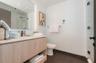 Floating wood-finish vanity with a rectangular sink, integrated LED mirror lighting, dark-toned floor tiling, and a glass-enclosed shower with subway 