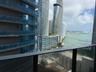 Balcony featuring metal railings with glass panels overlooking a bay, high-rise urban structures, and waterfront scenery