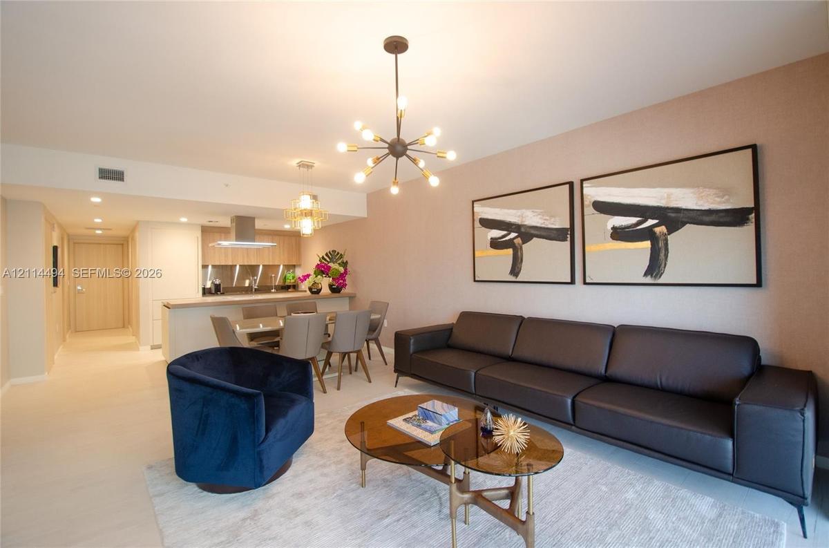 Open-concept living space featuring wood-finish flooring, a multi-arm sputnik-style chandelier, neutral wall tones, and a kitchen peninsula with integ