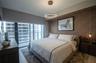 Floor-to-ceiling glass panel, textured accent wall, modern circular LED pendant lighting, dual hanging bedside fixtures, and neutral wood-finish floor