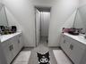 Dual vanity area featuring white cabinetry, light-toned stone-finish countertops, undermount sinks, wall-to-wall mirrors, and tile flooring