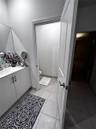 White vanity cabinet with a solid surface countertop, integrated sink, and modern metal hardware, complemented by tile flooring and a panel door