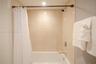 Shower and bathtub combination featuring large-format beige wall tiles, chevron-patterned accent tiling, a chrome wall-mounted shower head, and a chro