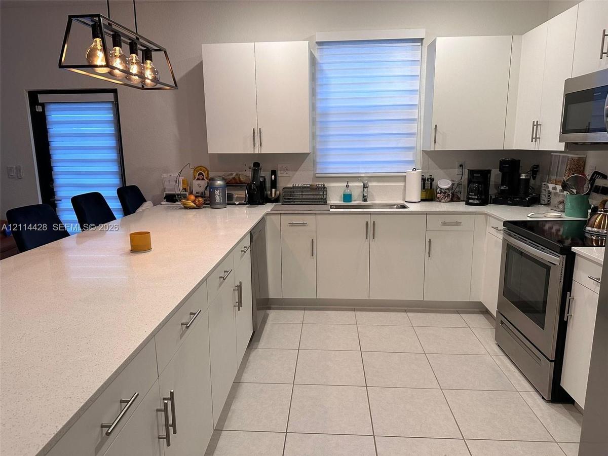 Kitchen featuring white flat-panel cabinetry, quartz countertops, an expansive island, tile flooring, and a rectangular geometric pendant light