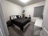 Neutral-toned carpeted flooring, white walls, and a window featuring dual-layer grey roller shades