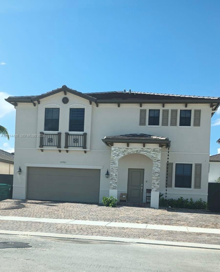 Two-story exterior featuring light-toned stucco, decorative stacked stone facade accents, two faux-balconies with railing detail, multi-pane windows w