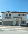 Two-story exterior featuring light-toned stucco, decorative stacked stone facade accents, two faux-balconies with railing detail, multi-pane windows w
