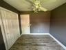 Wood-finish flooring, white paneled closet doors, six-panel interior door, and a ceiling-mounted light fixture with a fan