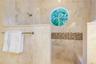 Walk-in shower featuring floor-to-ceiling stone tile, circular accent window, horizontal decorative stone inlay, built-in tiled bench, and wall-mounte