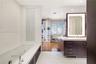 Contemporary bathroom featuring a deep-soaking tub with a tiled surround, custom dark-finish vanity cabinetry with a stone countertop, an integrated L