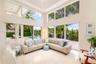 Double-height ceilings, floor-to-ceiling windows, polished stone flooring, and multiple sliding glass doors opening to a paved patio with a swimming p