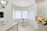 Kitchen nook featuring a bay window, white shaker-style cabinetry, stone-finish countertops, geometric metal pendant lighting, and neutral tile floori