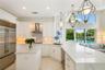 Kitchen featuring white cabinetry, quartz countertops, a stainless steel refrigerator, tile backsplash, and geometric pendant lighting