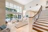 Double-height ceilings, floor-to-ceiling glass windows, staircase with wood-finish treads and metal railings, stone-faced interior column, and light-t