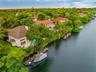 Waterfront estate featuring a private boat dock, tile roofing, an inground pool, and mature landscaping