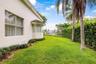 Stucco exterior featuring a bay window, expansive lawn, mature palm trees, and perimeter landscape hedging