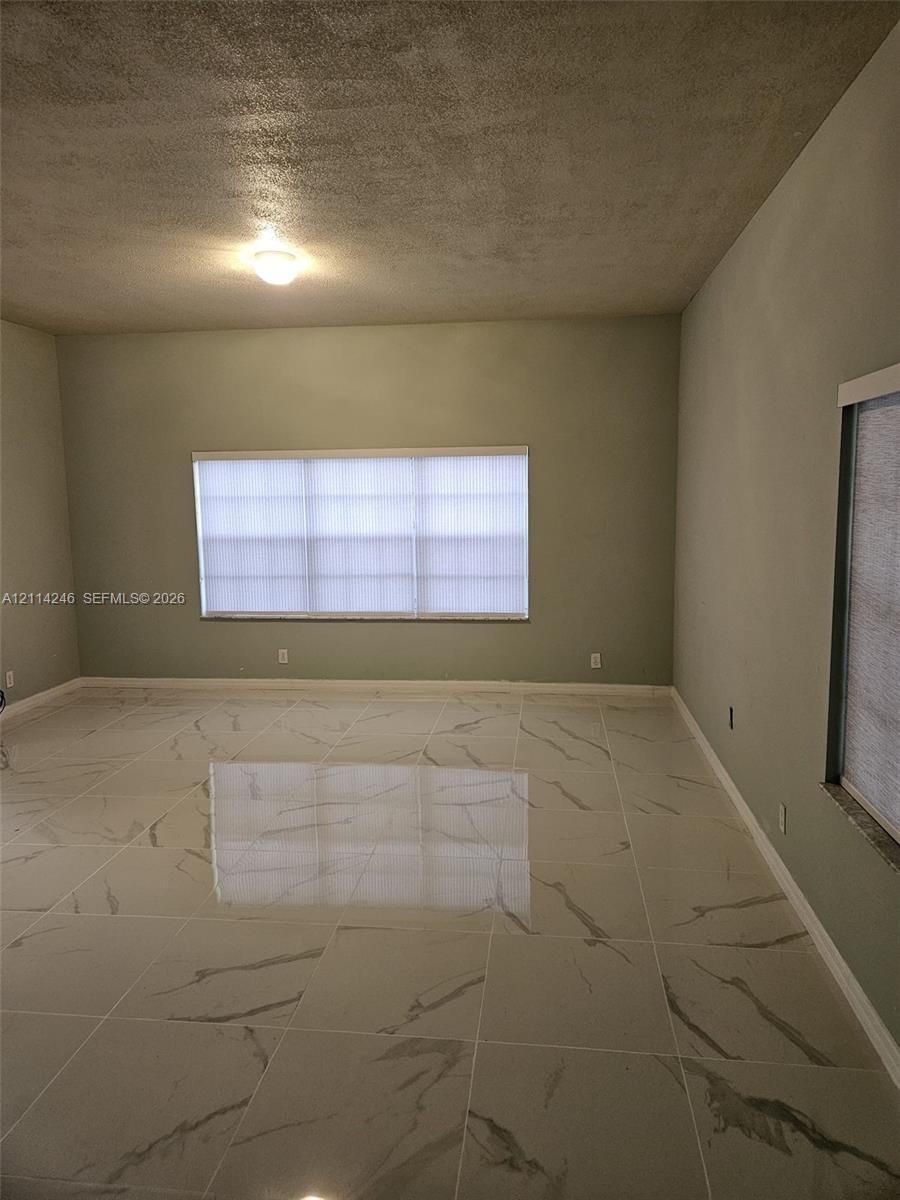 Interior room featuring large-format tile flooring with a veined pattern, neutral-toned wall paint, and windows with integrated blinds