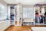 Custom closet featuring white built-in cabinetry, floor-to-ceiling mirrored doors, integrated window seating, plantation shutters, and wood-finish flo